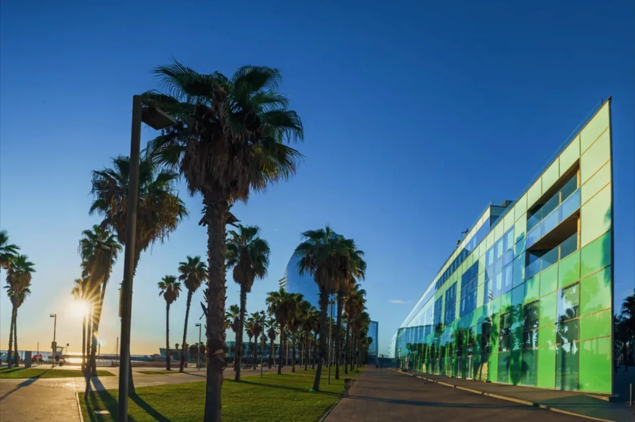 Norrsken House Barcelona, a green glass building behind palm trees.