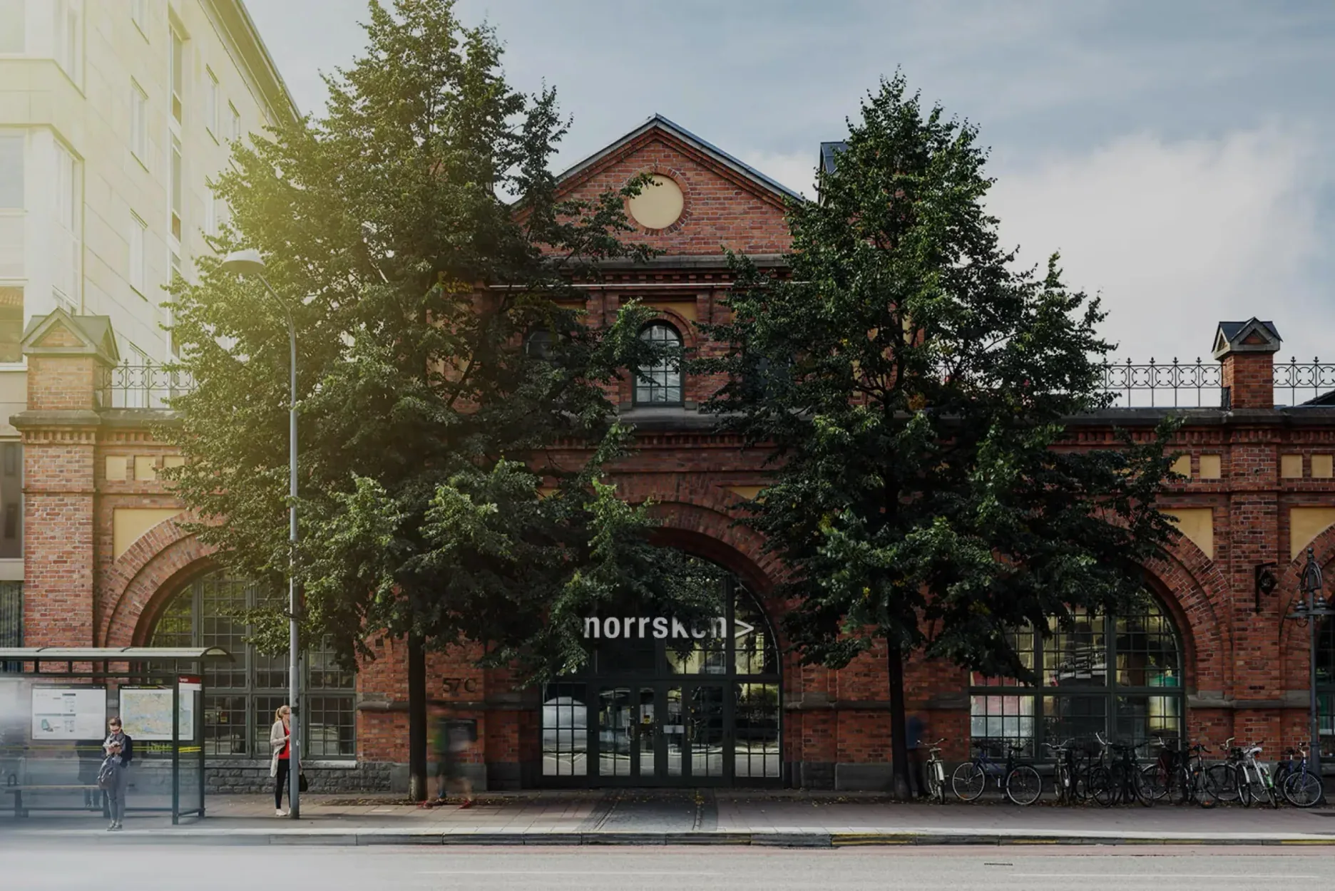 Norrsken House Stockholm, a red-brick former tram hall behind two linden trees.
